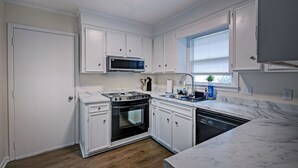Een keuken met witte kasten, een magnetron, fornuis, oven en vaatwasser.