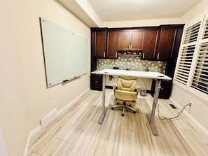 A home office with a desk, chair, whiteboard, wooden cabinets, and a window with blinds. - Chateau Sage Creek on the Lake, Hot Tub, Pool, Breathtaking sunsets, Nature path (Winnipeg)