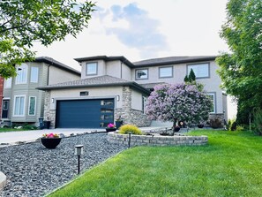 A two-story house with a stone facade, a dark garage door, and a well-maintained lawn. - Chateau Sage Creek on the Lake, Hot Tub, Pool, Breathtaking sunsets, Nature path (Winnipeg)