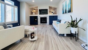 Una sala de estar moderna con chimenea, sofás blancos, una mesa de centro y un televisor montado en la pared.