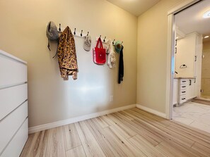 A hallway with a coat rack holding various items, a white dresser, and a wooden floor.