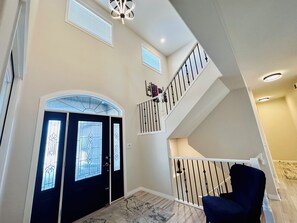 A multi-level home interior with a staircase, a black door with glass panels, and a blue chair.