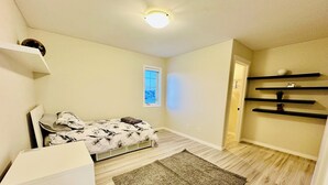 Een slaapkamer met een bed, een bureau, een raam en een inbouwplank.