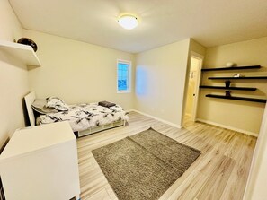 A bedroom with a bed, a desk, a window, and a built-in shelf.
