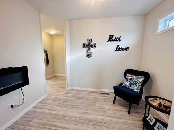 A living room with a TV mounted on the wall, a cross, and the words "Faith Love" on the wall.