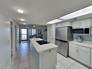 A modern kitchen with white cabinets, a stainless steel refrigerator, a microwave, and a coffee maker. - Windjammer 215 (St. Augustine)
