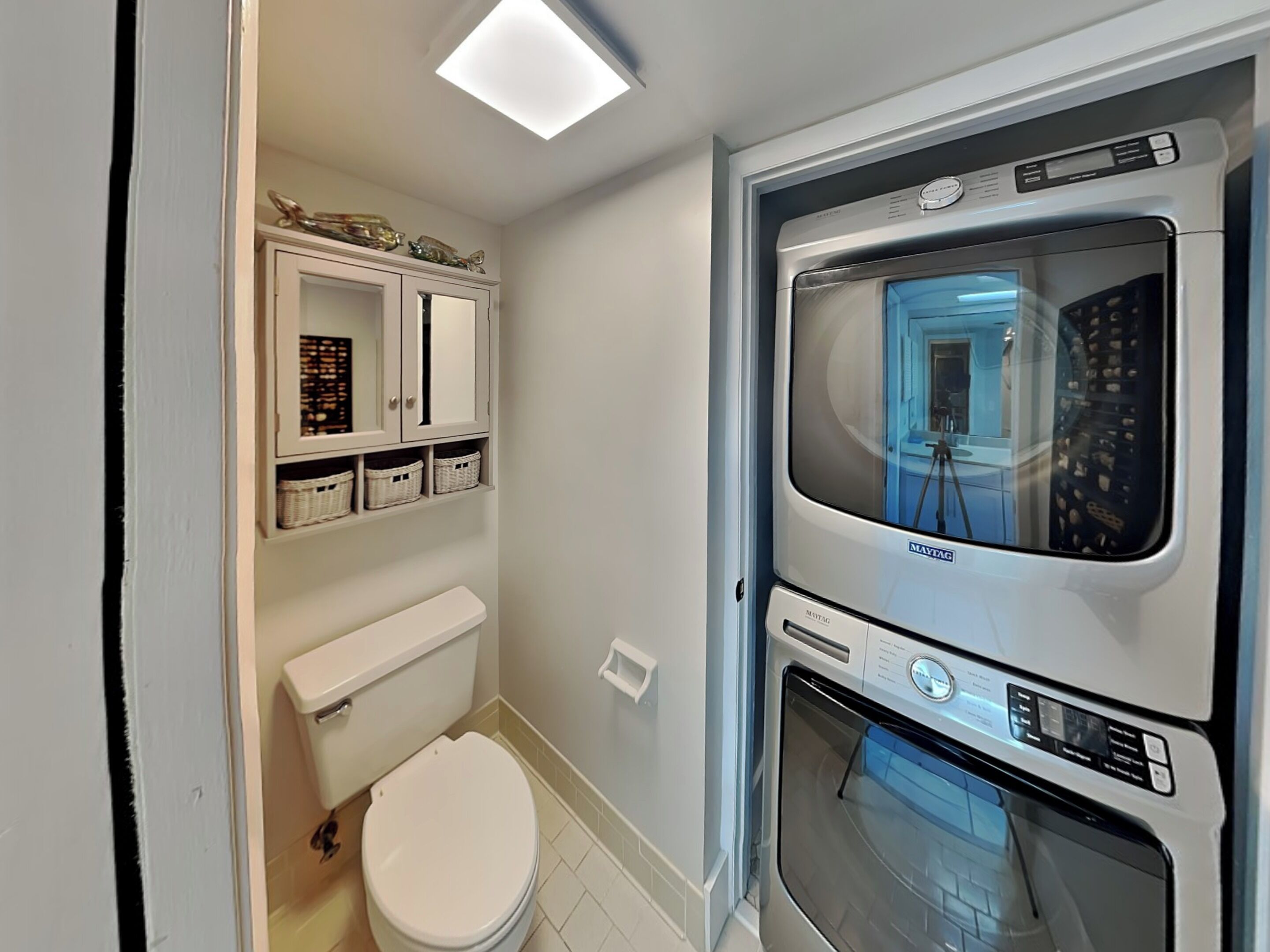 Un bagno compatto con il water, un mobile bianco con cesti e una lavatrice a incasso.
