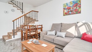 A living room with a staircase, a sofa, a dining table, and a painting on the wall. - Casa José: Mountain Views, Wi-Fi, and Air Conditioning in Nerja (Nerja)