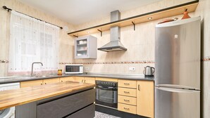 A kitchen with a stainless steel refrigerator, a built-in oven, a microwave, wooden cabinets, and a washing machine. - Casa José: Mountain Views, Wi-Fi, and Air Conditioning in Nerja (Nerja)