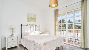 A bedroom with a bed, two bedside tables, a window with curtains, and a view of greenery outside. - Casa José: Mountain Views, Wi-Fi, and Air Conditioning in Nerja (Nerja)