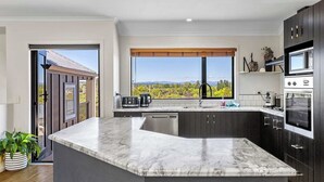 A modern kitchen with a large island, dark cabinetry, and a view of a vineyard through the window. - Rangatira Sunsets & Close to town (Taupō)