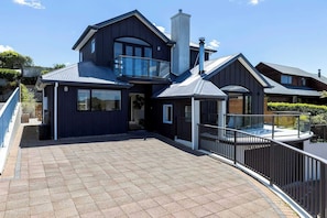 A modern two-story house with a balcony, large windows, and a tiled patio. - Rangatira Sunsets & Close to town (Taupō)