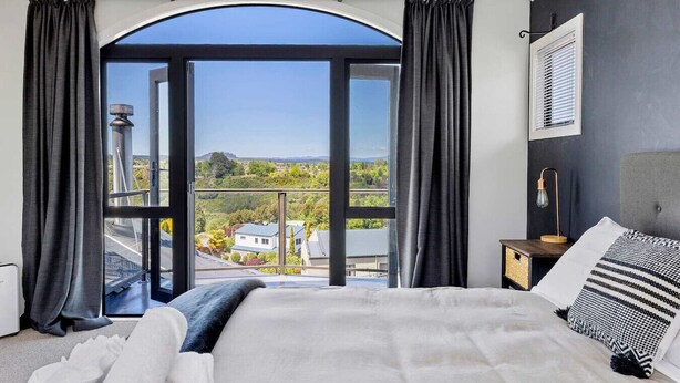 A bedroom with a large bed, a view of the countryside, and a window with curtains. - Rangatira Sunsets & Close to town (Taupō)