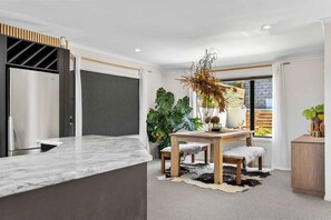 A modern kitchen with a marble countertop, a built-in oven, and a dining area with a wooden table and chairs. - Rangatira Sunsets & Close to town (Taupō)