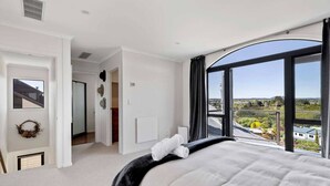 A bedroom with a large bed, a view of the countryside, and a door leading to another room. - Rangatira Sunsets & Close to town (Taupō)
