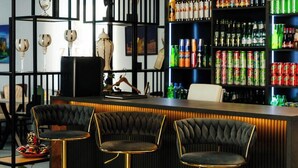 A bar area with three stools, a shelf with bottles, and a decorative wall with shelves. - Zafar Plaza Hotel (Namangan)