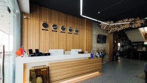 A modern hotel reception area with a wooden reception desk, clocks displaying different time zones, and a staircase leading to the upper floor. - Zafar Plaza Hotel (Namangan)