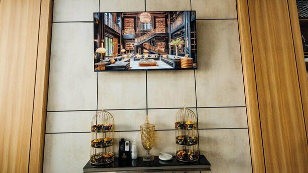 A wall-mounted television displaying a cityscape, a decorative floral arrangement, and a table with a vase and a tray of snacks. - Zafar Plaza Hotel (Namangan)