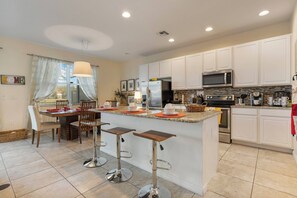 A modern kitchen with white cabinets, a central island with stools, a dining table with chairs, and a large window with curtains. - 4BR Pool Home w/ Lake View Bella Vida (Kissimmee)