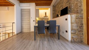 A dining area with a wooden ceiling, stone wall, and a TV mounted on the wall.