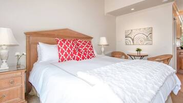 A neatly made bed with white and red patterned pillows, a wooden headboard, and a bedside table with a lamp.