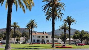 A large white building with a symmetrical facade, surrounded by well-maintained lawns and palm trees, set against a backdrop of hills. - Pet-Friendly Silverado Condos with Pool & Golf Course View (Napa)