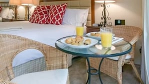 A hotel room with a bed, a dining table with breakfast, wicker chairs, and a large mirror. - Pet-Friendly Silverado Condos with Pool & Golf Course View (Napa)