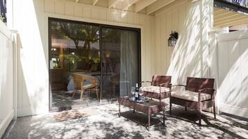 An outdoor patio with wicker furniture, a glass door leading to a room, and a white fence.