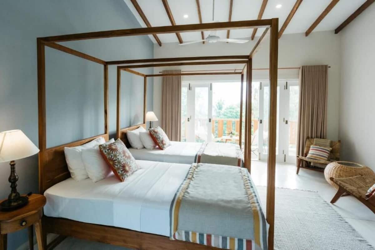 A four-poster bed with two pillows, a bedside lamp, and a wicker chair in a room with a balcony.