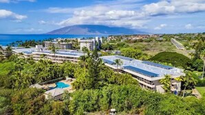 Ett semesterkomplex med flera byggnader, en swimmingpool och utsikt över havet och ett berg.