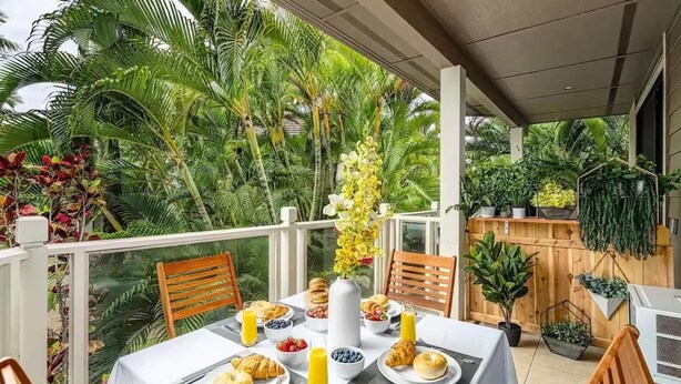 A balcony with a table set for breakfast, surrounded by lush tropical plants. - Spacious Ground Floor Maui Retreat, Grand Champion (Wailea-Makena)