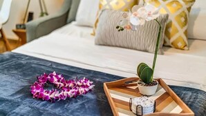 A neatly made bed with a grey and white duvet, a wooden tray with a potted plant and a decorative item, and a purple lei on a dark surface. - Spacious Ground Floor Maui Retreat, Grand Champion (Wailea-Makena)