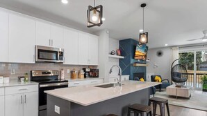 Une cuisine moderne avec des meubles blancs, un îlot central doté de tabourets, un four à micro-ondes et une cuisinière.