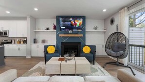 Un salon moderne doté d’un téléviseur à écran plat fixé au-dessus d’une cheminée, de deux canapés, d’une table basse et d’un fauteuil suspendu original.