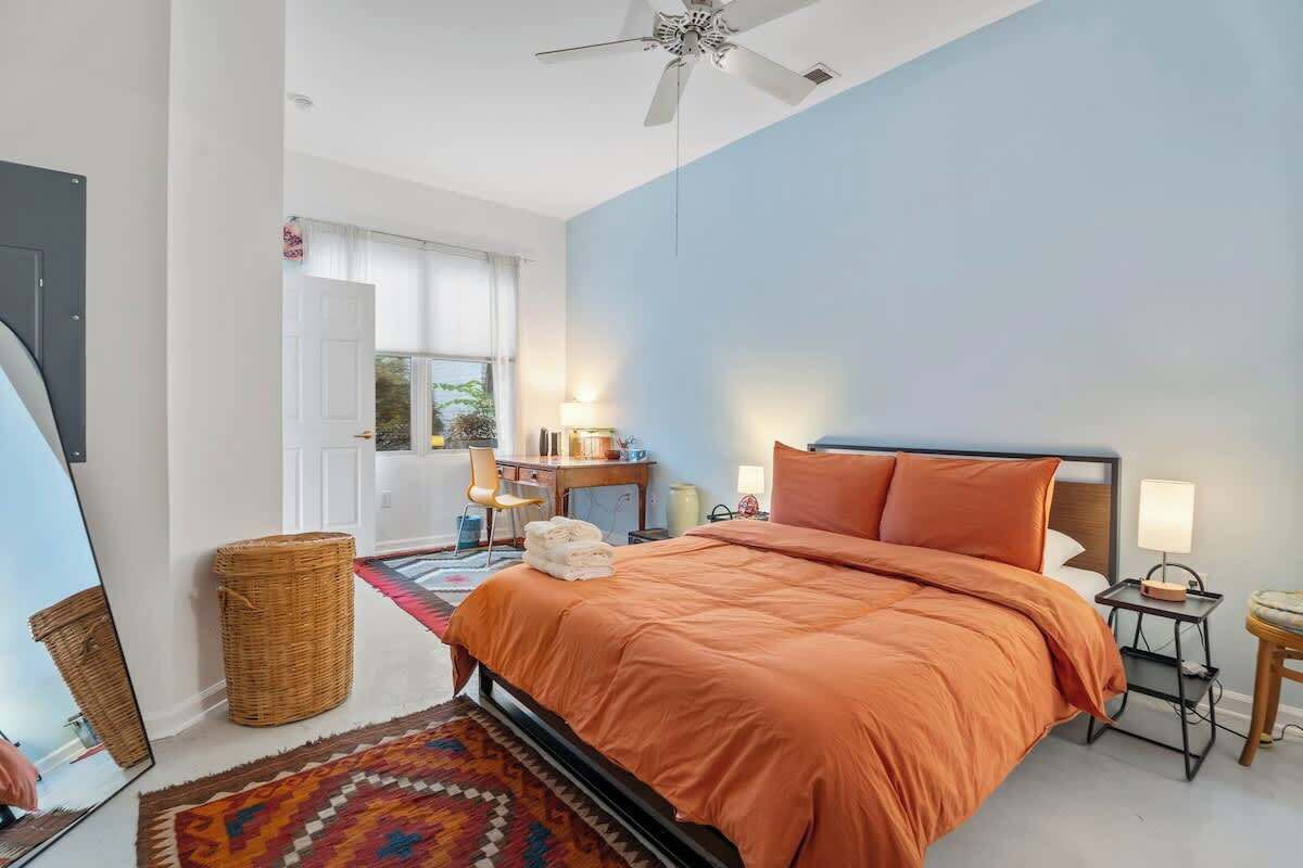 A bedroom with a bed, bedside tables, a ceiling fan, a window, and a door.