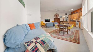 A living room with a sofa, a dining table with chairs, a kitchen area, and a large window. - Walkable Downtown Stay | Pet-Friendly & Spacious (Raleigh)
