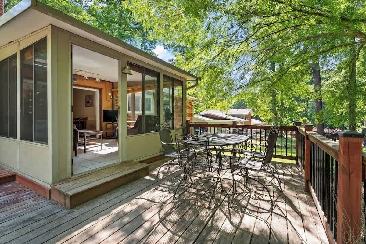 A covered patio with a table and chairs, a wooden deck, and a view of a house with a chimney.