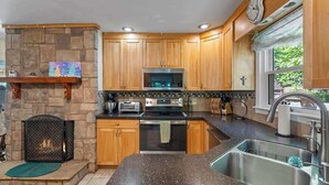 Une cuisine avec des meubles de rangement en bois, une cheminée en pierre, un évier en acier inoxydable et une horloge au mur.