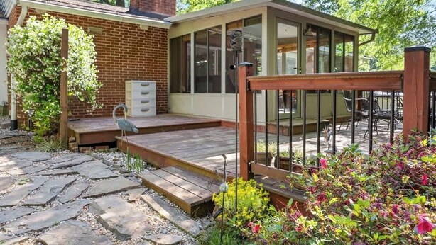 Un espace patio doté d’une terrasse en bois, d’un mur en briques et d’une structure vitrée.