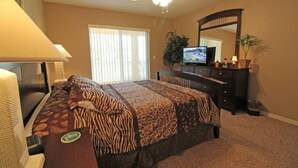 Een hotelkamer met een bed, een bureau, een televisie, een dressoir en een plafondventilator.