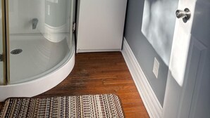 Ein Eckzimmer mit Duschkabine aus Glas, einem weißen Kühlschrank und einer Tür mit Kleiderhaken.
