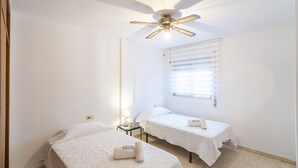 Una camera d'albergo con due letti singoli, una ventola a soffitto, un comodino con una lampada e una finestra con persiane.