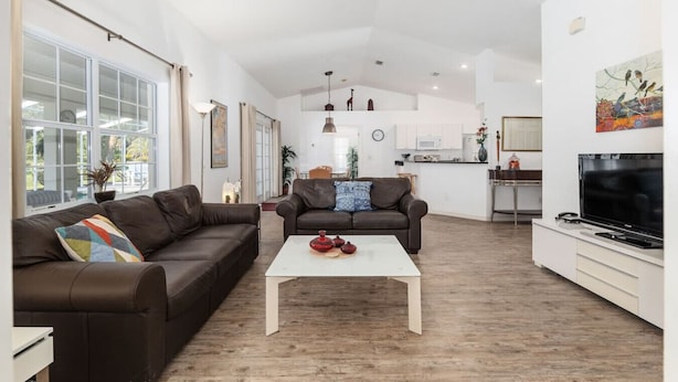 Amplia sala de estar con sofá, mesa de centro y televisor. Se observa una cocina al fondo.