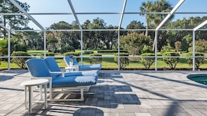 Un espacio de descanso al aire libre con sillones reclinables y una pequeña mesa, con vistas a un jardín cuidado y una piscina.