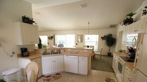 A compact kitchen with white cabinets, a coffee maker, and a dishwasher. There is a dining area with a table and chairs, and a refrigerator on the right. - 3 Bedroom & 2 bath with private pool (Hernando)