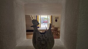 A ceramic vase in a narrow hallway with a view of a dining area and a window with a view of a red car outside.