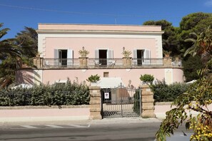 A two-story building with a pink facade, a balcony with potted plants, and a gated entrance. - VILLA FELICITA - SUNDIAL RESIDENCE (MARINA DI LEUCA)