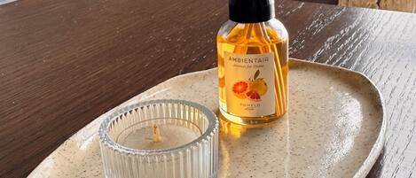 A ceramic tray with a glass candle holder and a bottle of AmbientaIR on a wooden table.