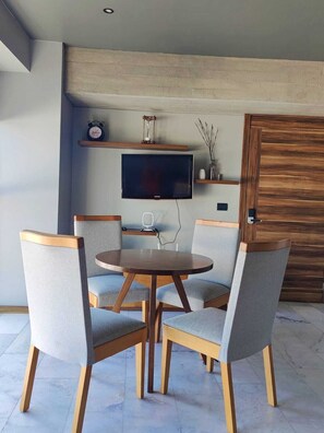 Een eethoek met een ronde tafel en vier stoelen, een flatscreen televisie aan de wand en een houten deur.