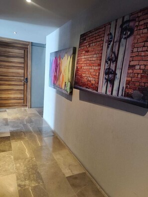 Een gang met een houten deur, een betegelde vloer en twee kunstwerken aan de muur.